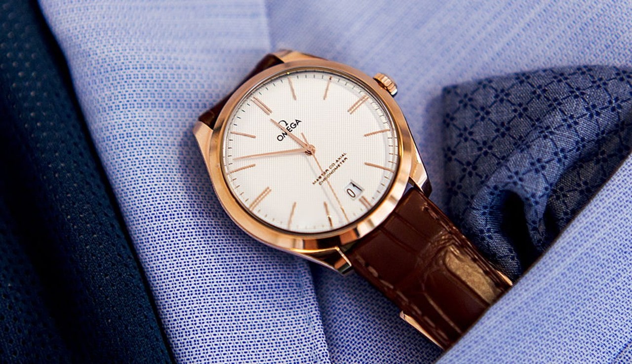 A close-up of a brown leather Omega wristwatch inside a lavender shirt pocket