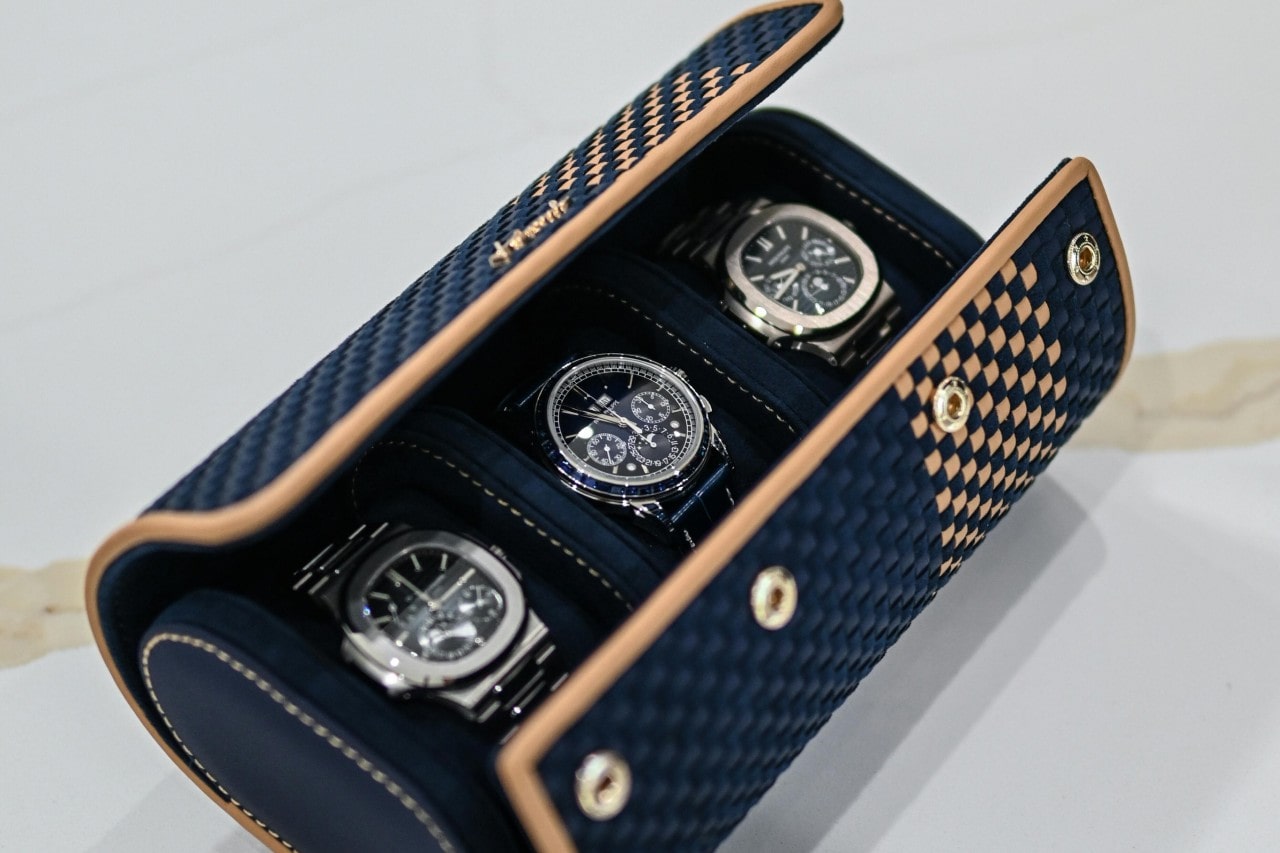 A dark blue watch holder with three metallic watches with black dials inside it.